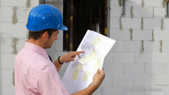 Bauherr liest Bauplan auf der Baustelle