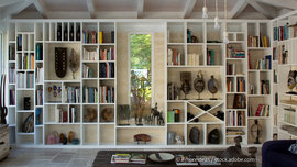 Bücher und Dekoelemente haben ihren vorgesehenen Platz in diesem individuellen Regal und werden somit zum Blickfang des Wohnbereichs. Besonderes Highlight hierbei ist das eingerahmte Fenster in der Mitte. (Foto: © #moreideas / stock.adobe.com) Massgefertigtes Regal für Bücher und Dekoration mit ausgesparten Fenster