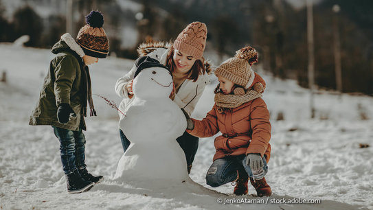 Eine Mutter baut mit Ihren zwei Kindern einen Schneemann