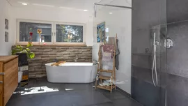 In unserem Haus Ibach wird ein Mix aus Steinoptik und großformatigen, dunklen Fliesen zum Hingucker. (Foto: © BAUMEISTER-HAUS) Badezimmer von Haus Ibach