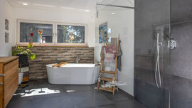 In unserem Haus Ibach wird ein Mix aus Steinoptik und großformatigen, dunklen Fliesen zum Hingucker. (Foto: © BAUMEISTER-HAUS) Badezimmer von Haus Ibach