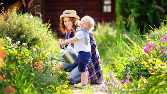 Frau und Kind gießen Pflanzen im Garten